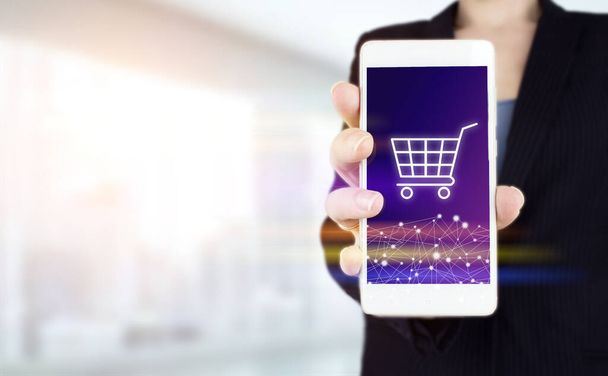 Internet Cart Web Store Online Buy E-Commerce concept. Hand hold white smartphone with digital hologram cart sign on light blurred background. Online shopping business technology internet concept - Photo, Image