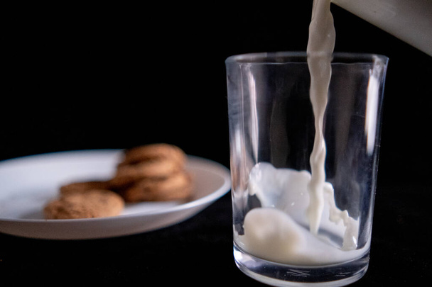 Verser le lait dans du verre à côté de la plaque de biscuits avec fond noir - Photo, image