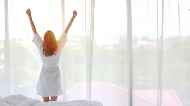 Зображення заднього виду хорошої форми і активної здорової молодої білої жінки, що прокидається вранці на сході сонця, стоячи і розтягуючись біля вікна в спальні
 - Фото, зображення