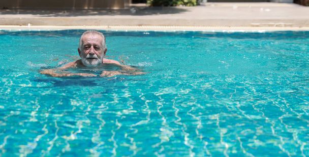 Felice anziano caucasico nuotare in piscina durante la vacanza di pensionamento con relax e sorridente. Vecchio avendo buon tempo in hotel all'aperto con il viso felice - Foto, immagini