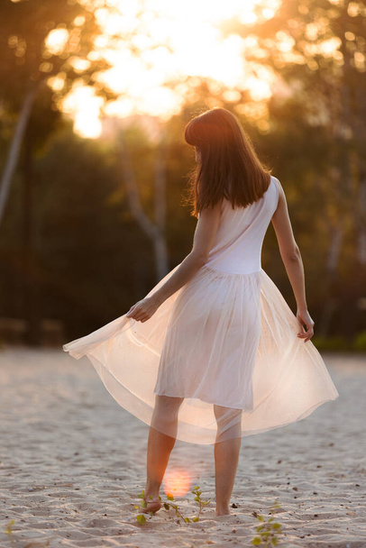 schöne junge modische Frau in elegantem Kleid, die bei Sonnenuntergang am Strand spaziert - Foto, Bild