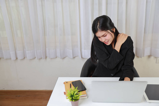 Młoda Azjatka zestresowana bizneswoman odczuwa ból lub ma problem z częścią ramienia lub szyi ciała po zbyt długim czasie pracy na komputerze. Koncepcja zespołu biurowego - Zdjęcie, obraz