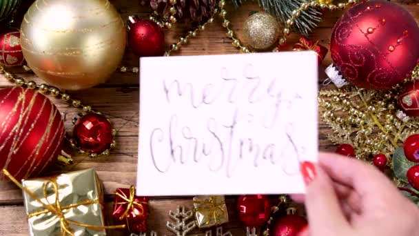Biglietto da donna con il testo scritto a mano MERRY CHRISTMAS card sul tavolo di legno con decorazioni natalizie da vicino - Filmati, video