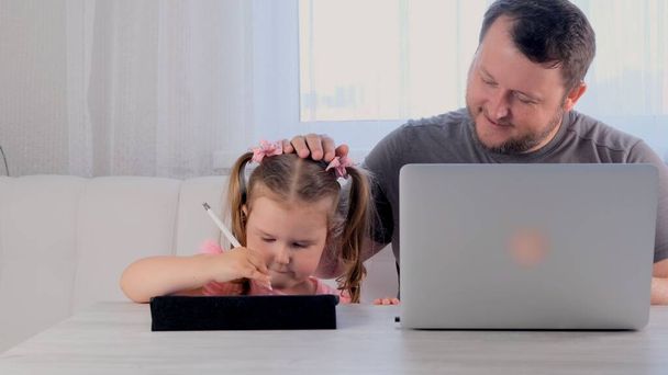 Bir iş adamının komik babası evinde, tablette oynayan 3 yaşındaki küçük bir kızın yanında dizüstü bilgisayarla çalışıyor. Modern aile. Serbest meslek kavramı. Aygıtlara bağımlılık - Fotoğraf, Görsel