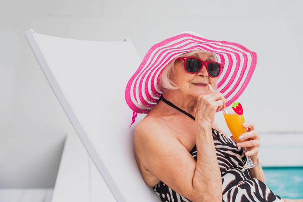 Happy senior woman having party in the swimming pool - Beautiful senior lady sunbathing and relaxing in a private pool during summertime - 写真・画像