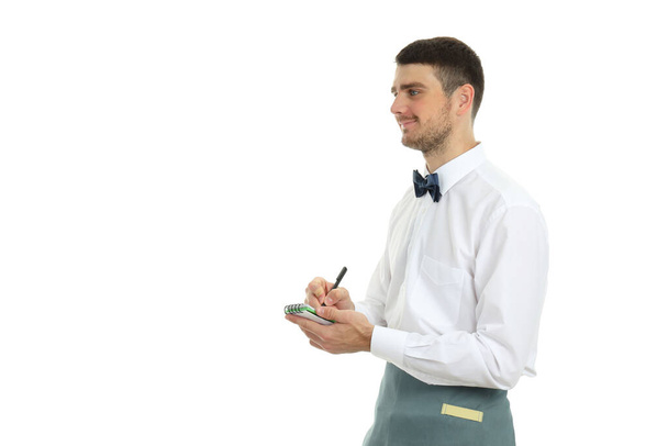 Νεαρός σερβιτόρος με σημειωματάριο και στυλό, απομονωμένος σε λευκό φόντο. - Φωτογραφία, εικόνα