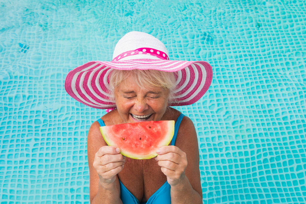 Happy senior woman having party in the swimming pool - Beautiful senior lady sunbathing and relaxing in a private pool during summertime - Foto, Imagem
