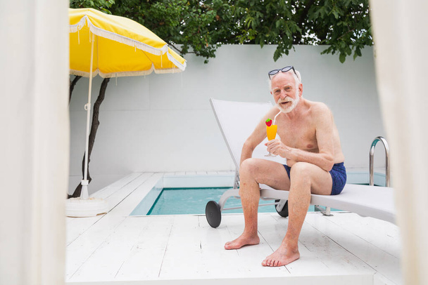 Happy senior man having party in the swimming pool - Active elderly male person sunbathing and relaxing in a private pool during summertime - Foto, imagen