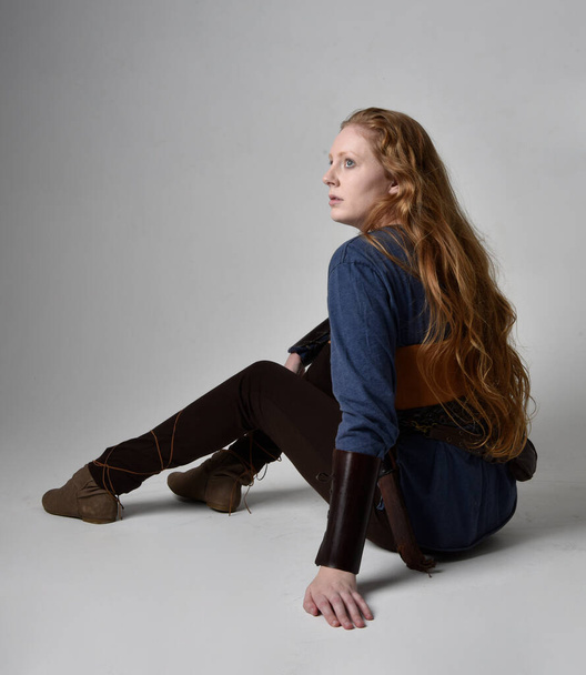 Orta çağ Viking ilham verici bir kostüm giyen, uzun bir kılıç taşıyan, stüdyo arka planında poz veren kızıl saçlı bir kadının tam boy portresi.. - Fotoğraf, Görsel