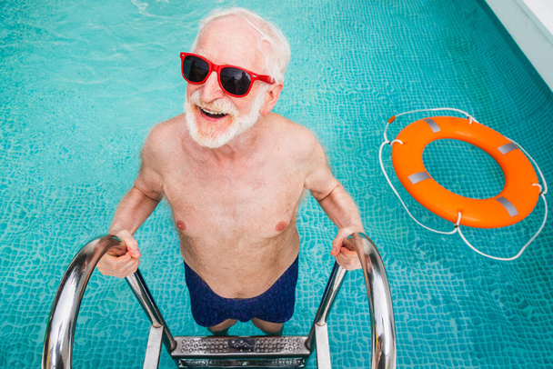 Happy senior man having party in the swimming pool - Active elderly male person sunbathing and relaxing in a private pool during summertime - Foto, Bild