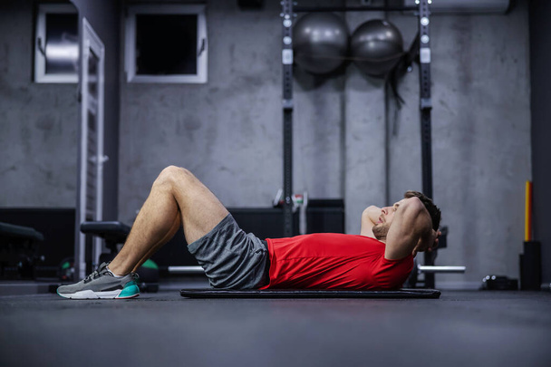 Un homme dans la salle de gym faisant des sit-ups. Le jeune homme en forme faisant un entraînement croquant pour améliorer ses abdos. Pompage des muscles abdominaux et renforcement du noyau du corps - Photo, image