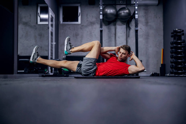 体形,腹部の筋肉の燃焼.男はジムの床に座り、精力的な動きをしています。健康的な方法で体重を失う,フィットネスルーチン - 写真・画像