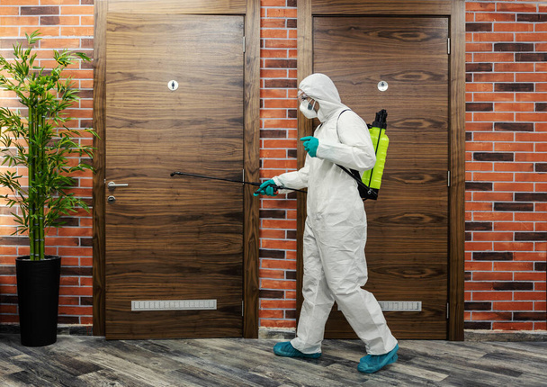 Stay healthy, warning for COVID 19. A male in a protective uniform prevents the spread of infection in a high-risk public place, restroom door disinfection. Coronavirus pandemic, antiseptic - Photo, Image