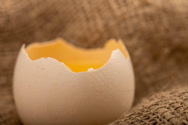 Разбитое белое куриное яйцо на домашней ткани с грубой текстурой, крупным планом избирательного фокуса - Фото, изображение