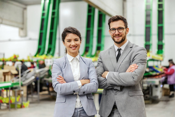 Portret van zakenmensen. Een man en een vrouw goed gekleed in een elegant pak poseren voor een foto in een bedrijfsomgeving in een fabriek. Positieve houding en glimlachend gezicht, zelfvertrouwen en carrière - Foto, afbeelding