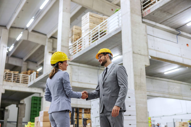 Successfully completed work. Man and a woman in business suits and hard hats shake hands and conclude a deal for the warehouse business Businesswoman and a businessman at work successfully make a deal - Valokuva, kuva