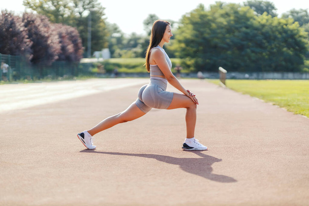 Vortreten, Beinmuskeln dehnen im Training. Eine Frau in enger grauer Fitnessbekleidung dehnt beim Sport ihre Beinmuskeln. Seitenhieb auf den hübschen Körper einer Frau beim Training - Foto, Bild