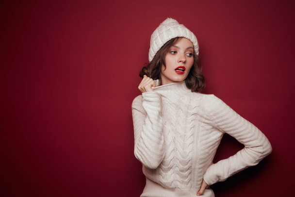 Dreamy woman in white knitted sweater hold collar on red background - Фото, зображення