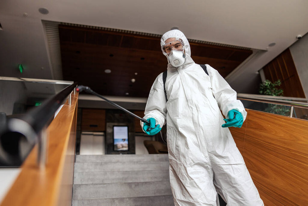 A photo of a man in a white uniform suppressing a coronavirus germ with a nozzle on closed public stairs. Stay healthy - Foto, Imagen