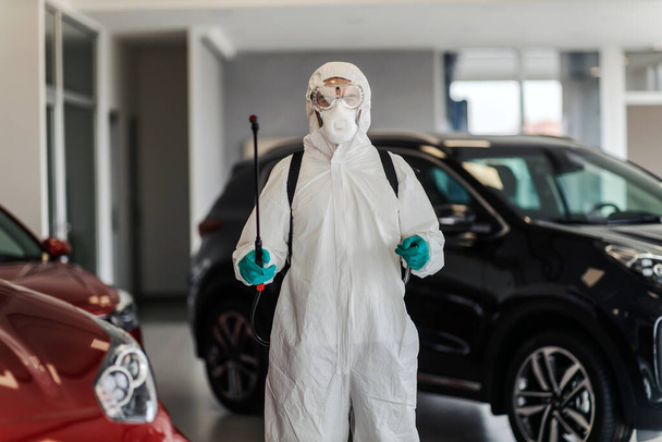 専門家は、重要なコロナウイルスの状況を警告します。保護服の男はアルコールとスプレーを使用しています。車のサロンでのスペースと空気の消毒。COVID19発生状況隔離 - 写真・画像