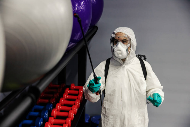 A COVID-19 vírus visszaszorítása és a tornatermi felszerelések tisztítása egy fehér öltönyös férfi által. A fotó középpontjában a pilates és a jógagolyók állnak. - Fotó, kép