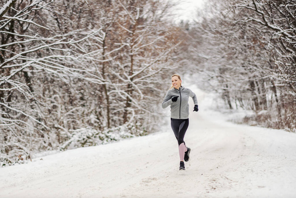 Sportswoman jogging in nature on snowy path at winter. Winter fitness, outdoor fitness, cardio exercises - Photo, Image