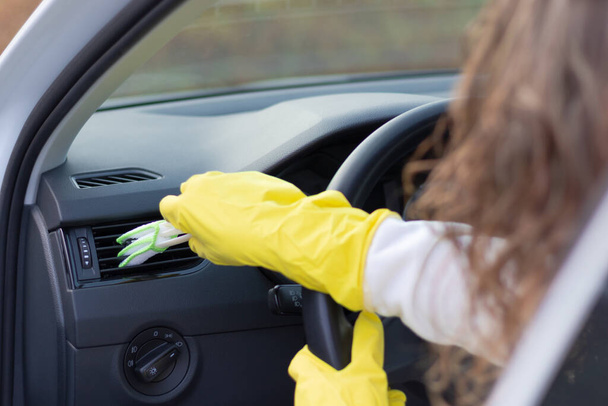 Dziewczyna w żółtych gumowych rękawiczkach wyciera deskę rozdzielczą samochodu z kurzu specjalną szczotką w jasny jesienny dzień. Wybiórcze skupienie. Zbliżenie - Zdjęcie, obraz