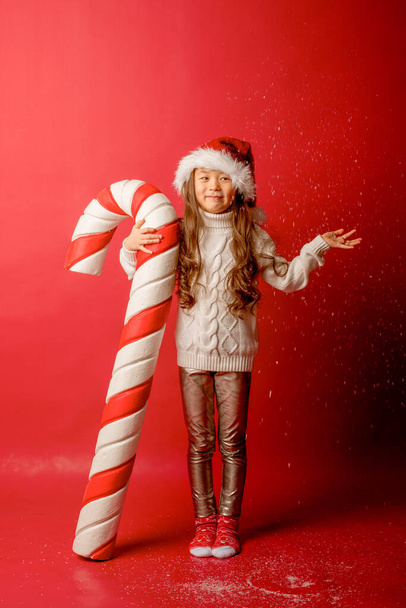 chica asiática chica en santa hat en un grifo el fondo con un gran caramelo para coger la nieve - Foto, Imagen