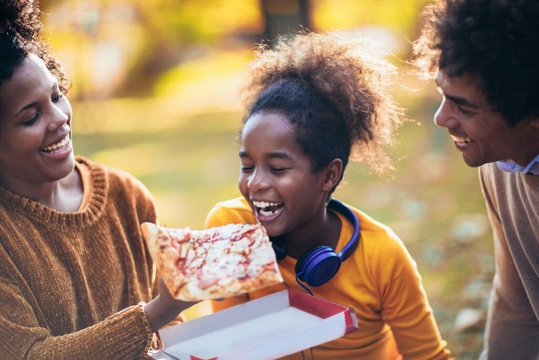 Familia mixta divirtiéndose mientras hace picnic en el parque comiendo pizza. - Foto, imagen