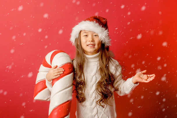 meisje aziatische meisje in kerstman hoed op een kraan de achtergrond met een groot karamel naar vangen de sneeuw - Foto, afbeelding