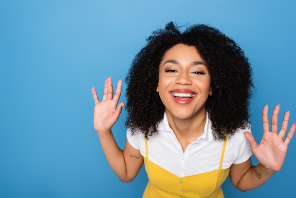cheerful african american woman smiling at camera and waving hands isolated on blue - Foto, imagen