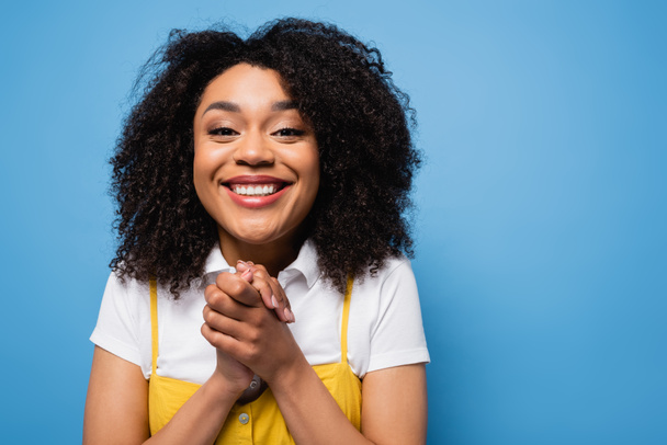 excited african american woman with clenched hands smiling at camera isolated on blue - Foto, imagen