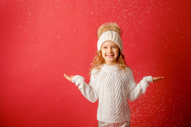 girl in a knitted hat catches snow on a red background - Foto, immagini