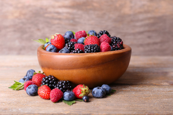Ripe sweet different berries in bowl, on old wooden table - Фото, изображение