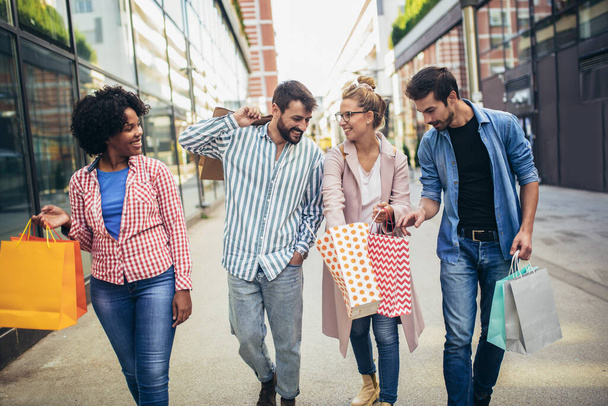 Grupa przyjaciół spacerujących ulicą z torbami na zakupy i zabawy. - Zdjęcie, obraz