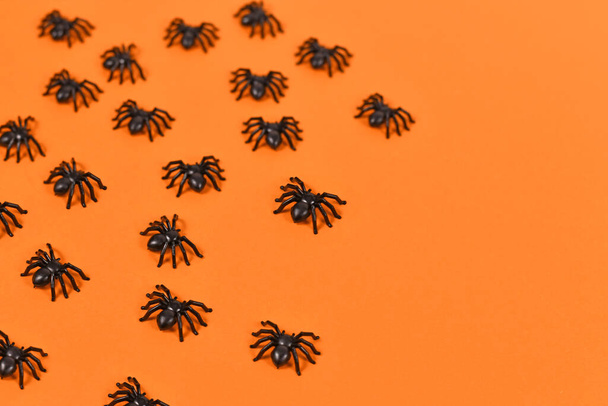 Small black plastic spiders creeping over orange Halloween background with copy space - Фото, изображение