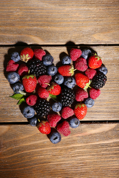 Heart of ripe sweet different berries, on old wooden table - Foto, Bild