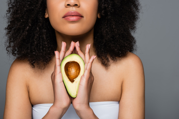 обрізаний вид афроамериканської жінки в білому верхньому тримає половину авокадо ізольовано на сірому
 - Фото, зображення