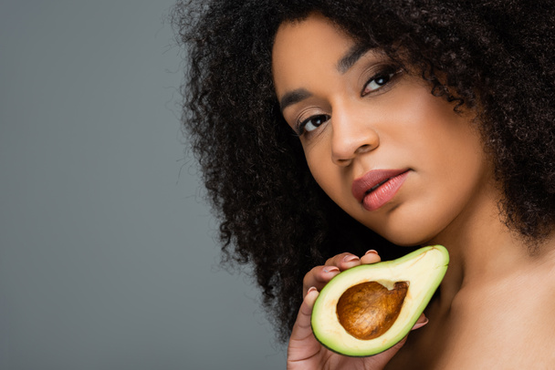 young african american woman with natural makeup holding half of fresh avocado isolated on grey - Valokuva, kuva