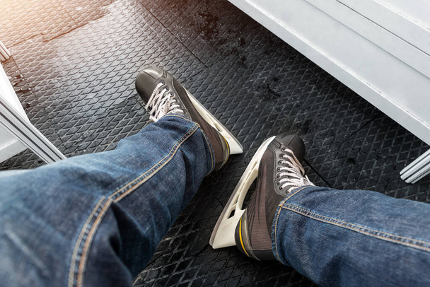 Close-up detail view of male person legs wearing jeans and black rental skating boots standing on non-slip rubber soft mat in dressing room locker skating rink. Healthy recreation leisure activity - Foto, immagini