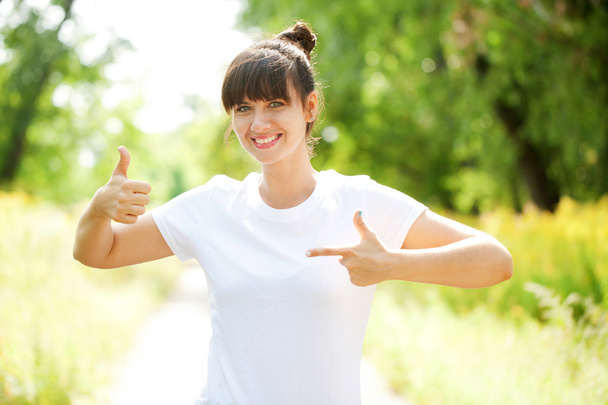 Mujer con camiseta blanca mostrando un pulgar hacia arriba
 - Foto, imagen