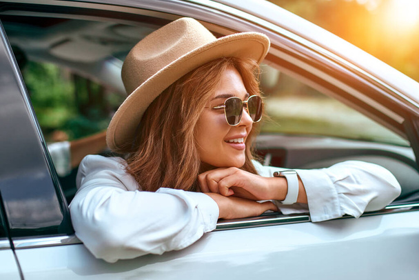 Egy nő kalapban és napszemüvegben kinézett a kocsi ablakán és ellazult. Kocsit veszek. Utazás, turizmus, kikapcsolódás. - Fotó, kép