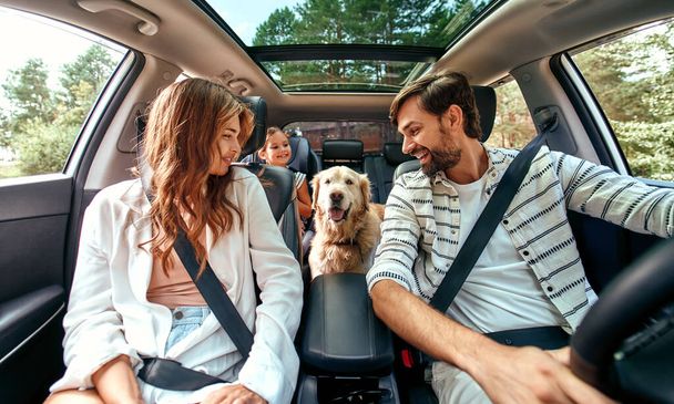 Cała rodzina jedzie na weekend. Mama i tata z córką i pies Labrador siedzą w samochodzie. Wypoczynek, podróże, turystyka. - Zdjęcie, obraz