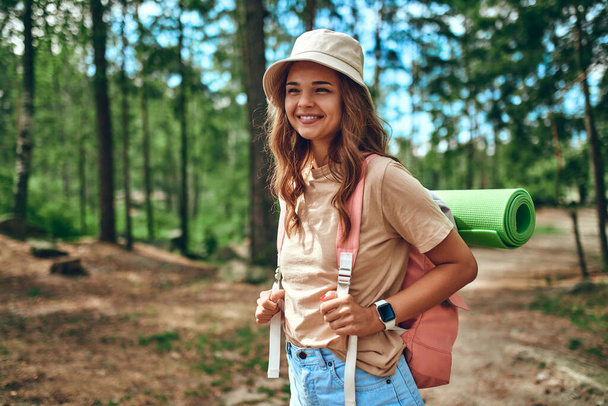 Nainen vaellus hattu ja reppu seisoo taustaa vasten metsän. Retkeily, matkailu, vaellus. - Valokuva, kuva