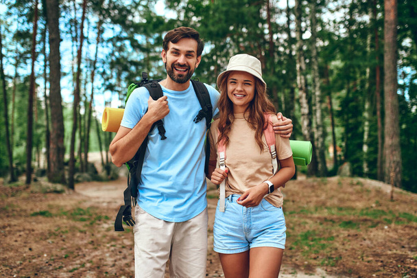 A loving couple of hikers stand with backpacks on the background of the forest. Camping, travel, hiking. - Foto, Imagen