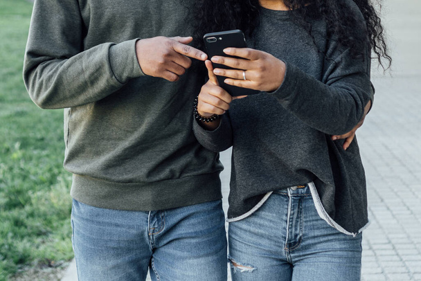Jeune couple regardant du contenu sur un téléphone portable tout en marchant ensemble à l'extérieur dans la rue. - Photo, image
