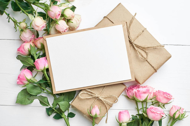 Greeting card mockup with fresh roses and gift boxes on white wooden background, card with copy space - Photo, image