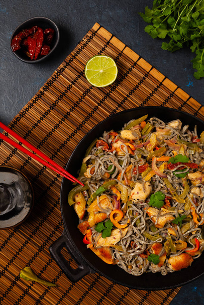 Wheat noodles with black sesame, fried in a wok with chicken and vegetables. Top view. - Fotó, kép