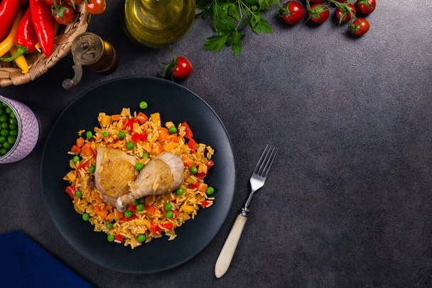 Arroz con pollo. Baked pieces of chicken with bone, rice with paprika and peas. Black background. Served on black plate or spanish pan.  - Foto, immagini