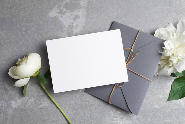 Ευχετήρια κάρτα ή κάρτα πρόσκληση mockup με αντίγραφο χώρου και φάκελο με λευκά λουλούδια παιώνιος σε γκρι - Φωτογραφία, εικόνα
